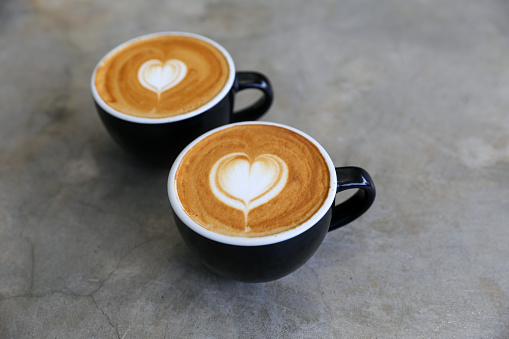 Two hot cups of cappucino on concrete background. Heart shape art latte symbol of love. Valentine's day concept