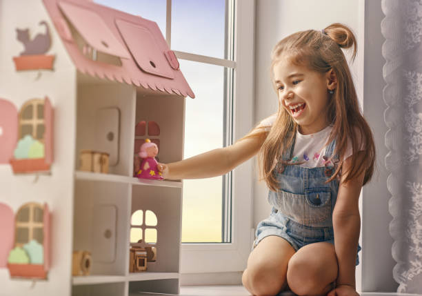 girl plays with doll house Happy girl plays with doll house and teddy bear at home. Funny lovely child is having fun in kids room. girl playing with doll stock pictures, royalty-free photos & images