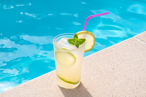 Fresh lemonade or mojito cocktail in glass with straw on a swimming poll border on sunny day