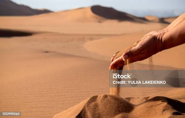 Closeup Hand Releasing Dropping Sand Sand Flowing Through The Hands Against Golden Desert Stock Photo - Download Image Now