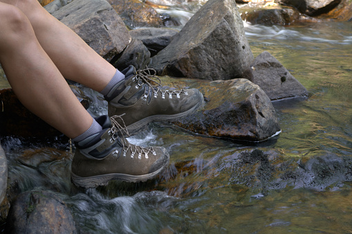 Woman sits on the stone in the stream. Close up legs in hiking boots image