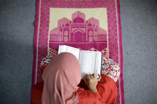 A Muslim girl is reading Quran (koran - holy book).