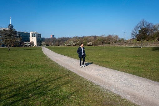 Young man in stylish blue shaded clothing walking and standing in public park on sunny day