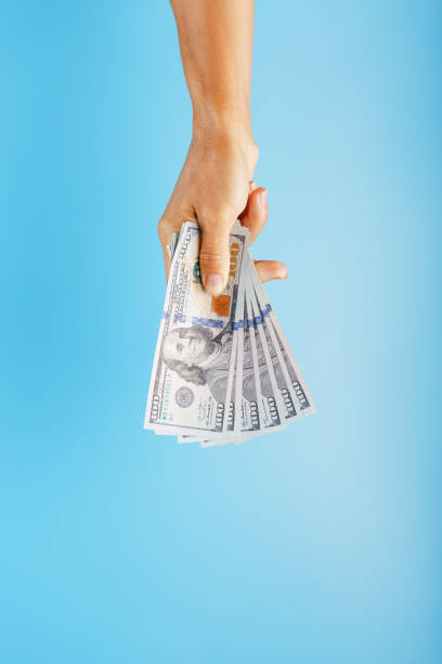 istock A hand with one hundred-dollar bills on a blue background. 1312950935
