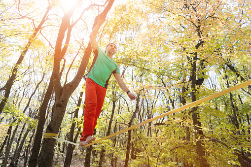 Autumn forest. middle aged athletic man practices slackline balance in autumn forest