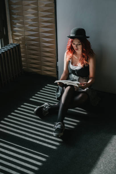 A young student in school uniform sitting on a floor and reading a book