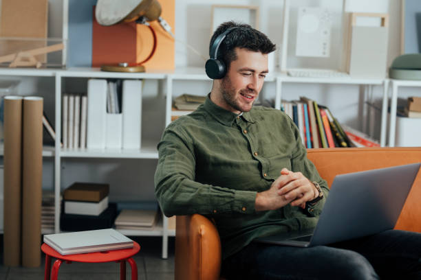 istock Modern Working Stations: a Smiling Freelancer Sitting in the Office with Headphones on and Listening to Music While Working on his Laptop 1312953562
