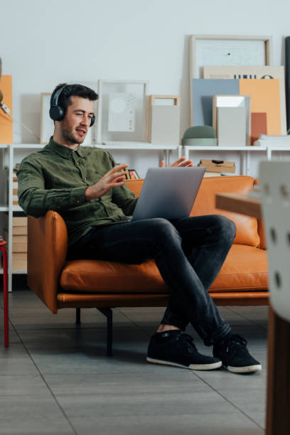 istock Modern Working Stations: a Smiling Freelancer Sitting in the Office with Headphones on and Listening to Music While Working on His Laptop PC 1312953568