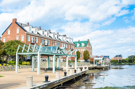 Benches under sylish metal gazebos on an empty riverside footpath on a sunny autumn morning. New brick row houses are in background. Alexandria, VA, USA.