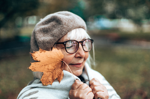 Caucasian romantic woman in french warm beret, glasses and woolen blanket enjoys in the park, autumn day