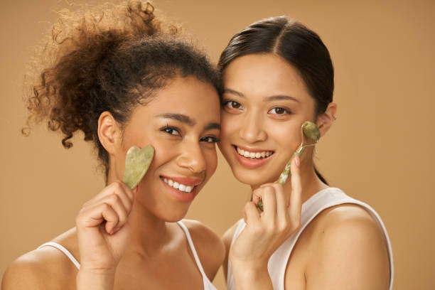 istock Cute young women smiling at camera, using jade roller and facial gua sha while posing together isolated over beige background 1312958374