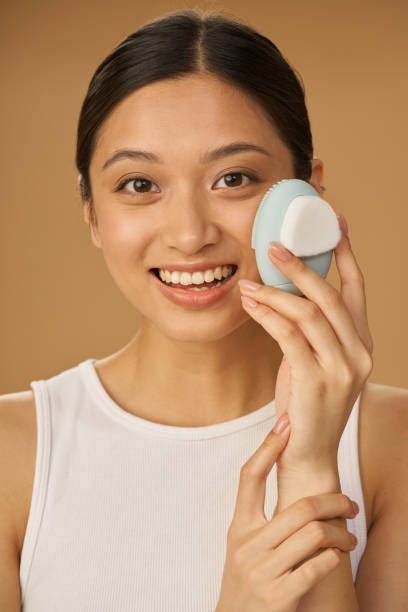 istock Excited young woman smiling at camera while using silicone facial cleansing brush, posing isolated over beige background 1312958381