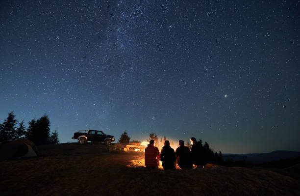 夜の星空の下でキャンプファイヤーの近くに座っているハイカーのグループ。 - friendship camping night campfire ストックフォトと画像