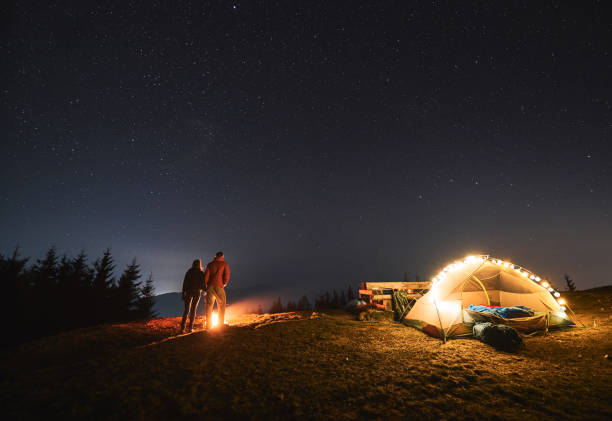istock Young couple hikers standing near campfire under night starry sky. 1312962936