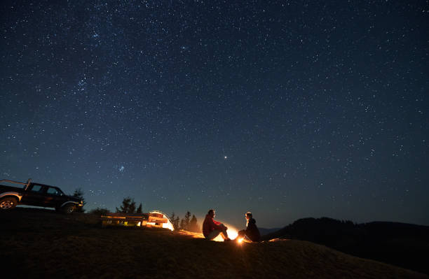 istock Young couple hikers sitting near campfire under beautiful night sky. 1312962937