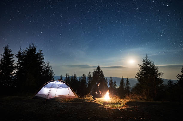 istock Male hiker looking at bright campfire under night starry sky. 1312963028