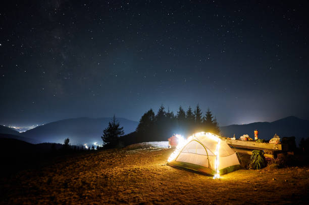 istock Hiker sitting near illuminated camp tent under night starry sky. 1312963767