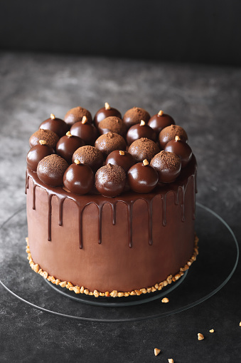 Contemporary Chocolate Truffle Layer Cake with chocolate smudge, decorated with handmade chocolate truffles, on a dark gray background.