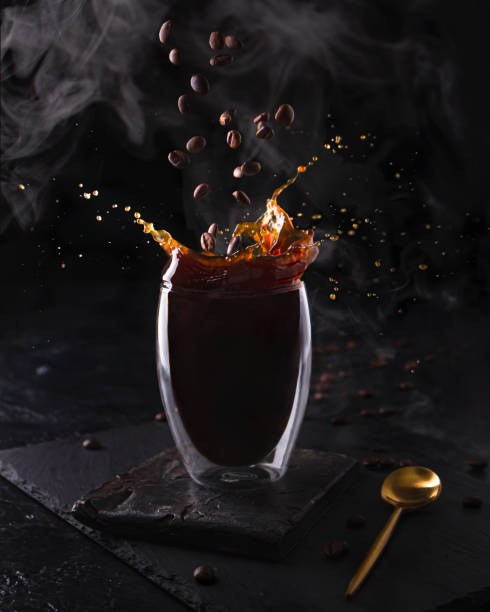 istock Hot espresso morning coffee in glass cup. Fragrant drink splashes with falling down coffee beans and steam on black background. Banner design 1312968461