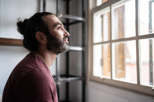 hombre mirando a través de la ventana en casa - esperar fotografías e imágenes de stock