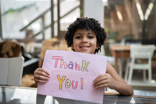 Girl holding paper with 'thank you' written at home