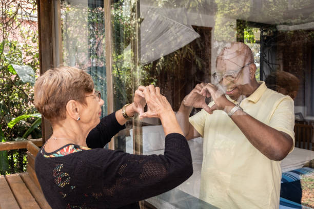 istock Senior couple separeted during quarantine doing heart shape with hands through the window 1312971165