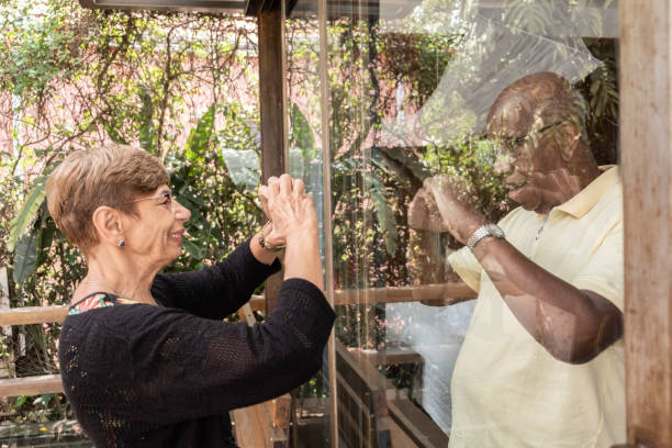 istock Senior couple separeted during quarantine doing heart shape with hands through the window 1312971166
