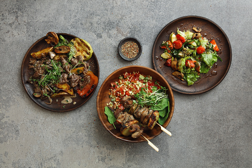 Skirt steak with grilled vegetables. Turkey skewers and bulgur salad. Vegetable salad. Flat lay top-down composition on concrete background.
