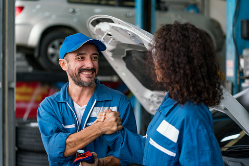 Two happy auto mechanics in uniforms working in auto service with car. Two men handshake mechanics in auto repair service.