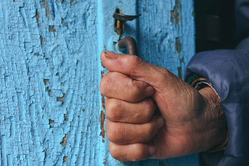 Old hand with dirty nails on door handle of wooden door