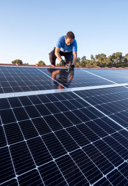 Professional worker installing solar panels on the roof of a house. Kneeling professional fixing solar panels from the top of a house roof, close-up front view solar power station solar panel house solar energy stock pictures, royalty-free photos & images