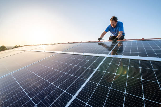 Professional worker installing solar panels on the roof of a house. Kneeling professional fixing solar panels from the top of the roof of a house, side view of the roof with sun reflection close-up control panel stock pictures, royalty-free photos & images
