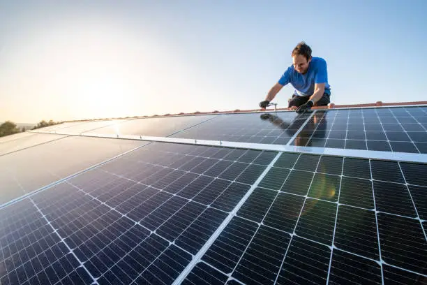 Kneeling professional fixing solar panels from the top of the roof of a house, side view of the roof with sun reflection close-up