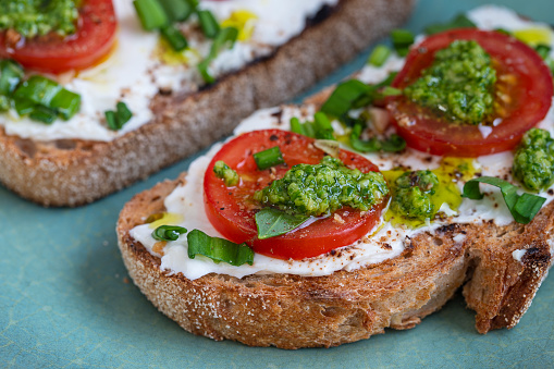 Delicious toasted bread with white cream cheese, green wild garlic and red tomato on plate, close up