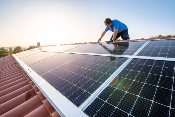 Professional worker installing solar panels on the roof of a house. kneeling professional fixing solar panels from the top of a house roof, side view of the roof with sun reflection Solar Energy stock pictures, royalty-free photos & images