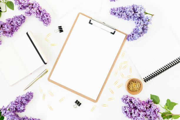 istock Home office composition with clipboard, diary, lilac flowers and accessories on white background. Flat lay, top view. 1312982722