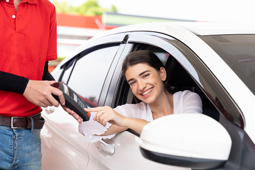 Woman customer paying by credit card with happy and smile at gas station. Refuelling car and service payment with wireless bank payment terminal concept