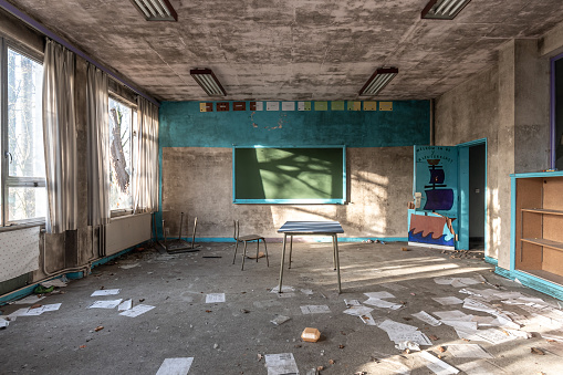 Abandoned classroom in soft tones, view of chalkboard and chaos of papers