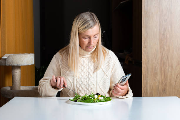 istock middle aged blonde woman  using smartphone while eating salad in the kitchen 1312988966