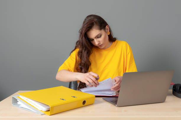 jeune femme d’affaires avec le long cheveu foncé travaillant avec le document dans le bureau, isolé sur le fond gris - paper document pen long hair photos et images de collection