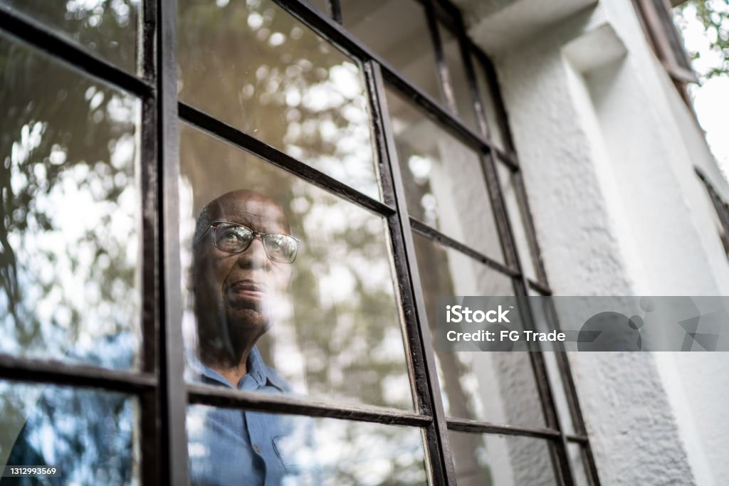 Senior man looking through the window at home Senior Adult Stock Photo