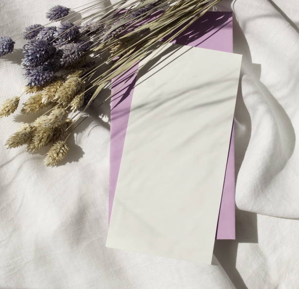 istock Card mockup and envelope with copy space top view.Still life composition, flat lay.Greetings, wedding invitations blank, and dry purple flowers with sunlight shadow on white linen fabric background. 1312995301