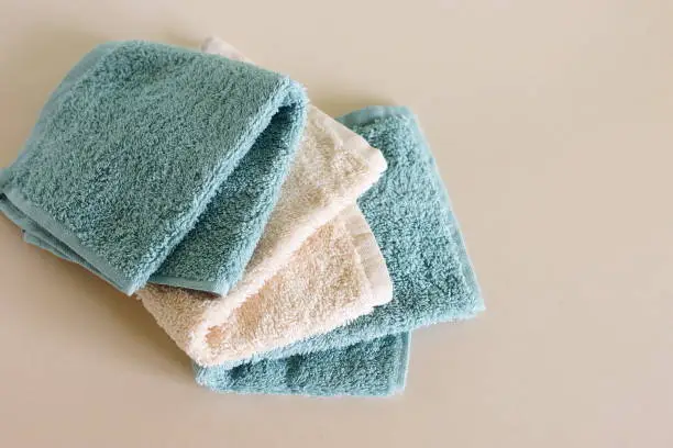 Set of beige and green soft terry towels on beige background top view  copy space. Bathroom accessories backdrop.