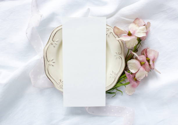 istock Wedding menu mockup card with copy space top view. Still life composition, flat lay. Greetings,  invitations blank, ribbon and pink flowers ranunculus on white linen fabric background. 1312999217