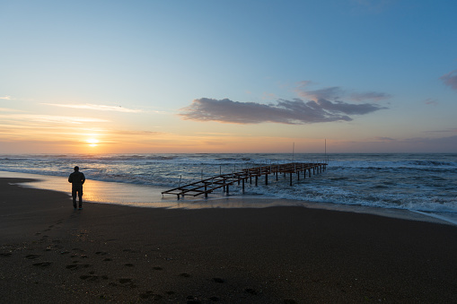 A man by the sea during the sunrise next to a pier structure