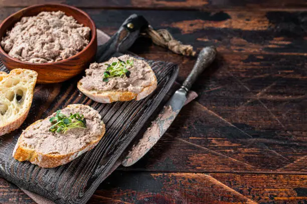 Photo of Toasts with Duck pate Rillettes de Canard on wooden board. Dark wooden background. Top View.  Copy space