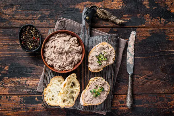 Photo of Toasts with Duck pate Rillettes de Canard on wooden board. Dark wooden background. Top View