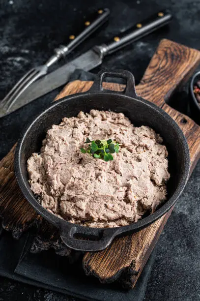 Photo of Duck pate Rillettes de Canard in a pan with greens. Black background. Top View