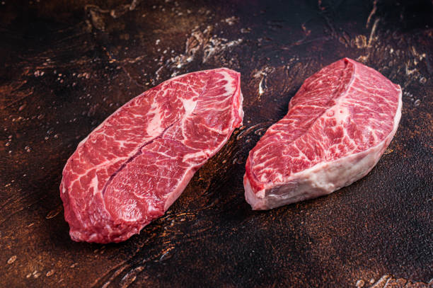 Raw Top Blade or flat iron beef meat steaks on a butcher table. Dark background. Top View Raw Top Blade or flat iron beef meat steaks on a butcher table. Dark background. Top View. boneless chuck steak stock pictures, royalty-free photos & images