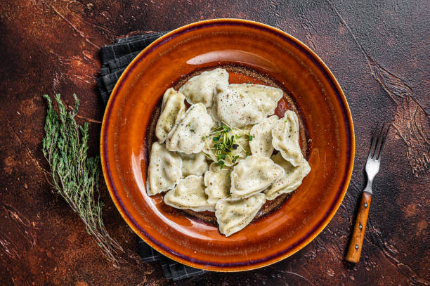 Polish Pierogi Dumplings with potato in a plate with herbs and butter. Dark background. Top View Polish Pierogi Dumplings with potato in a plate with herbs and butter. Dark background. Top View. russian pelmeni stock pictures, royalty-free photos & images